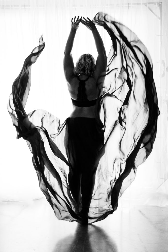 Blonde woman in gorgeous black and white photo throwing silk fabric in the air showing body-positivity