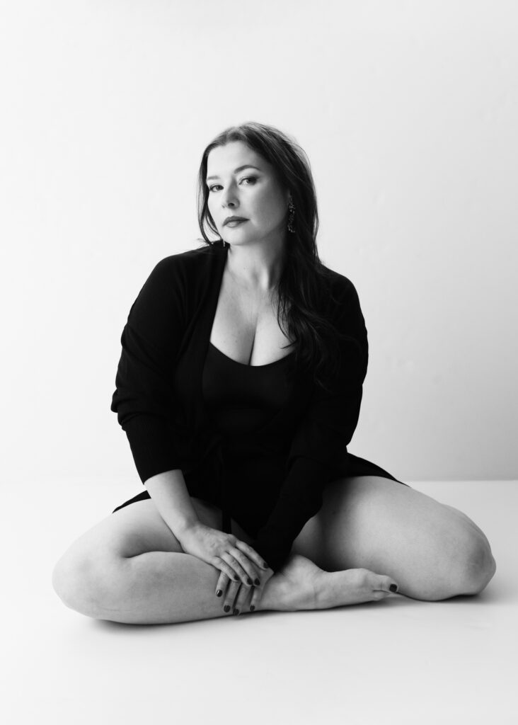 Black and white photo of a dark haired woman sitting on the floor for her body image journey photoshoot